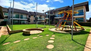Un patio con un parque infantil, columpios y un camino circular de piedra rodeado de edificios.