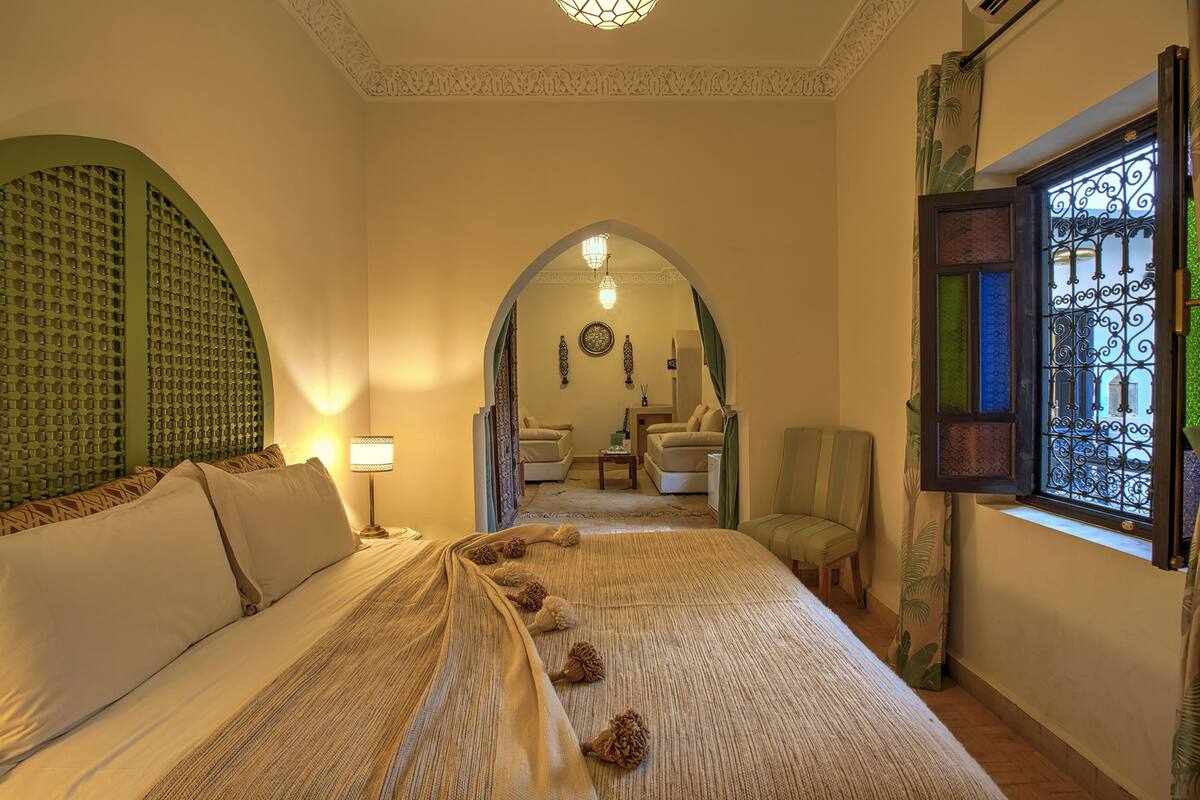 A hotel room with a large bed, a sitting area with a sofa and chairs, and a decorative arched doorway leading to another room.