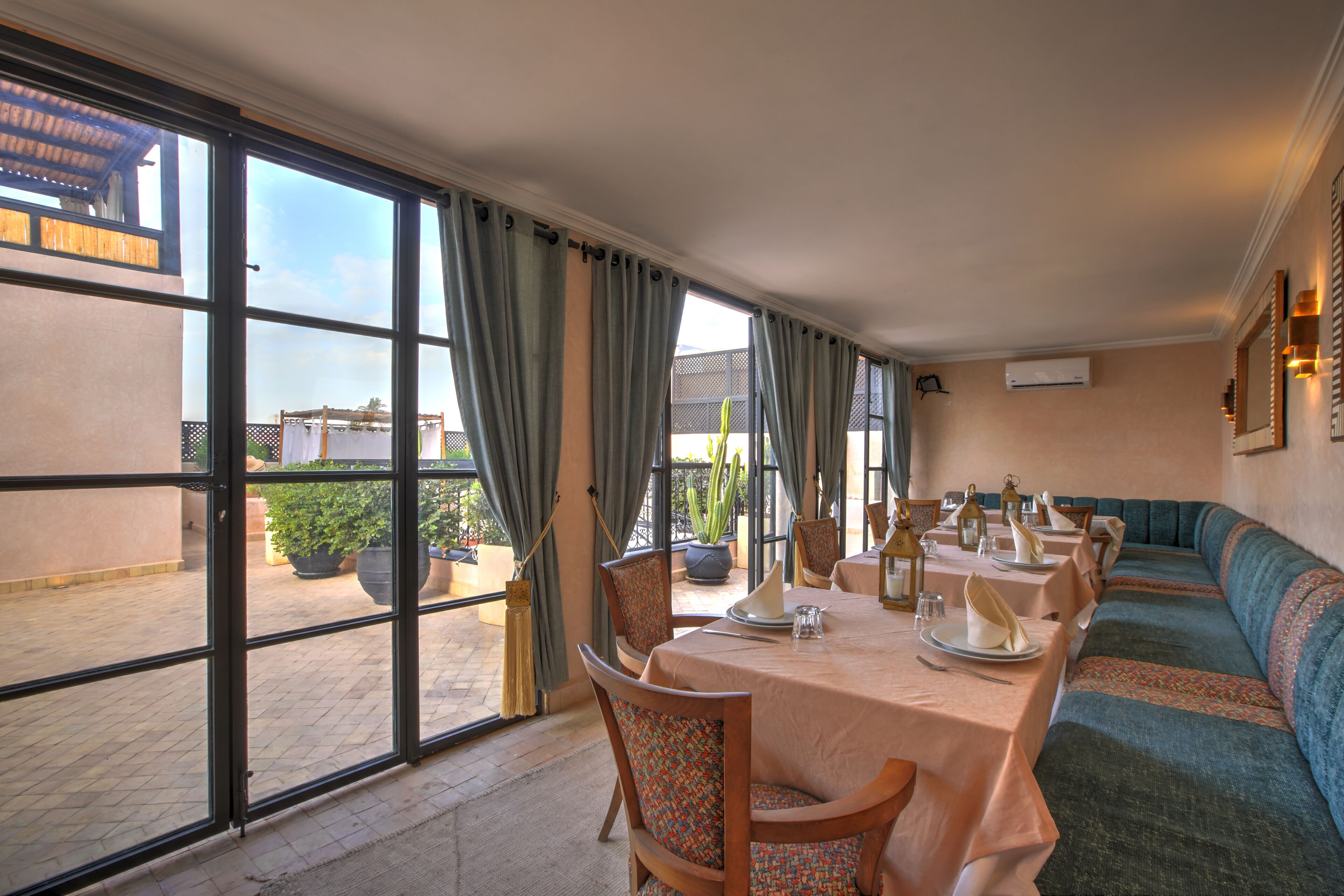 A dining area with a long table set for a meal, large windows with curtains, and a view of the outside.