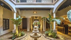 A courtyard with a central fountain, surrounded by plants and columns, leading to a covered area with a pool and seating. - RIAD BIJOUX (Marrakech)