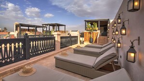 A rooftop terrace with wicker lounge chairs, a decorative fence, and wall-mounted lanterns. - RIAD BIJOUX (Marrakech)