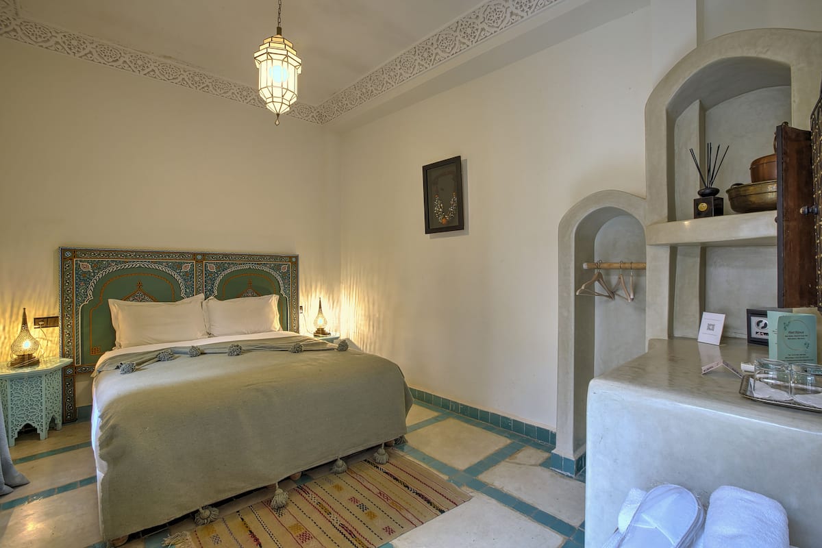 A bedroom with a bed, a nightstand, a hanging lamp, a wall-mounted shelf, and a mirror.
