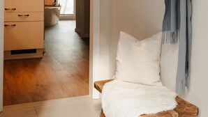 A room with a wooden chair, a white sofa, and a wooden coat rack with a grey scarf. - Apartment between forest and lake with free-standing bathtub and balcony (5 star DTV) (Ratzeburg)