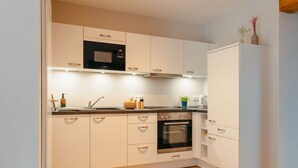 A modern kitchen with white cabinetry, a built-in oven, and a microwave. - Apartment between forest and lake with free-standing bathtub and balcony (5 star DTV) (Ratzeburg)