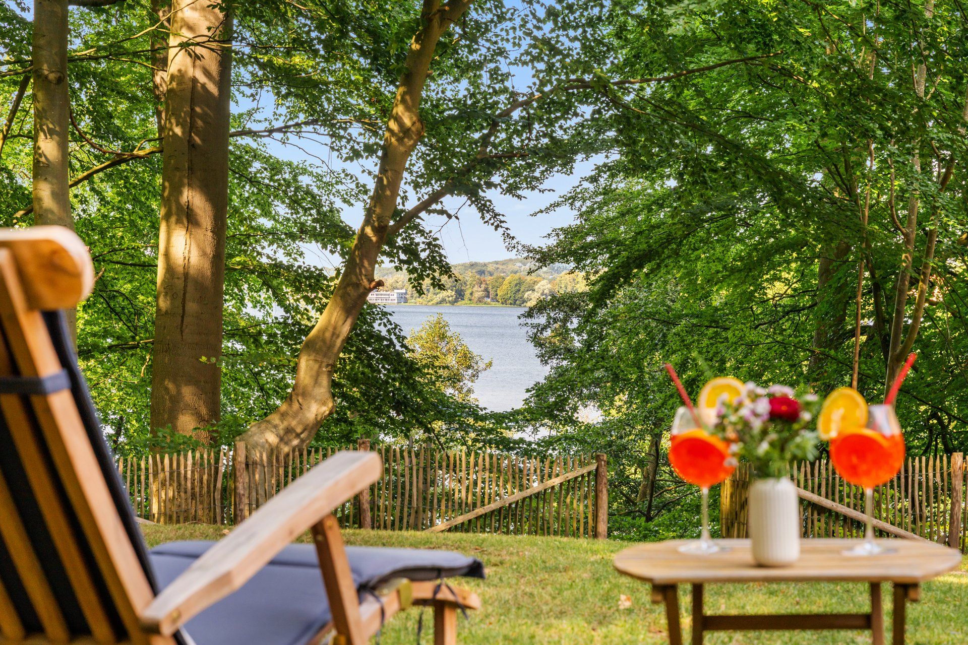Eine Holzterrasse mit Seeblick, ein hölzerner Zaun und ein Tisch mit einem Blumenstrauß.