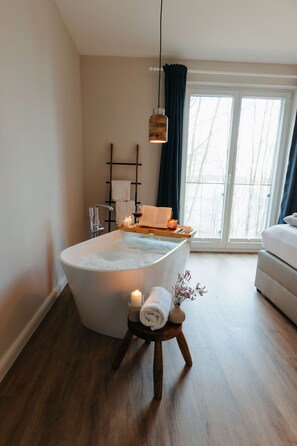 Un bagno moderno con una vasca freestanding, uno sgabello di legno con un asciugamano e una finestra con tende.
