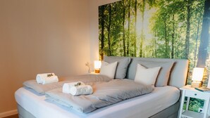A modern bedroom with a large bed, a nightstand, a wall-mounted lamp, and a wooden floor. - Apartment between forest and lake with free-standing bathtub and balcony (5 star DTV) (Ratzeburg)