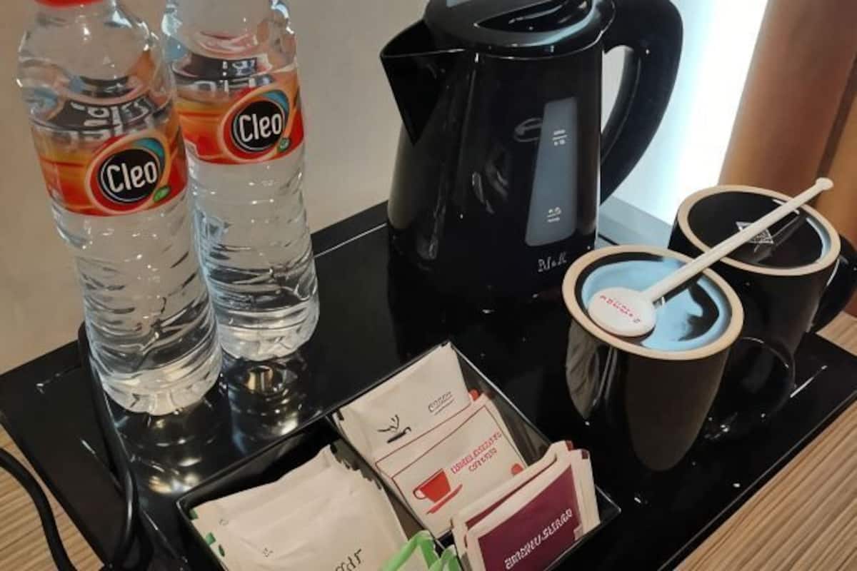 Uma cafeteira, duas garrafas de água, duas chávenas e alguns pacotes de café numa bandeja.
