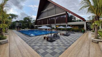 Un edificio moderno con un techo triangular distintivo, una piscina y zonas de estar al aire libre.