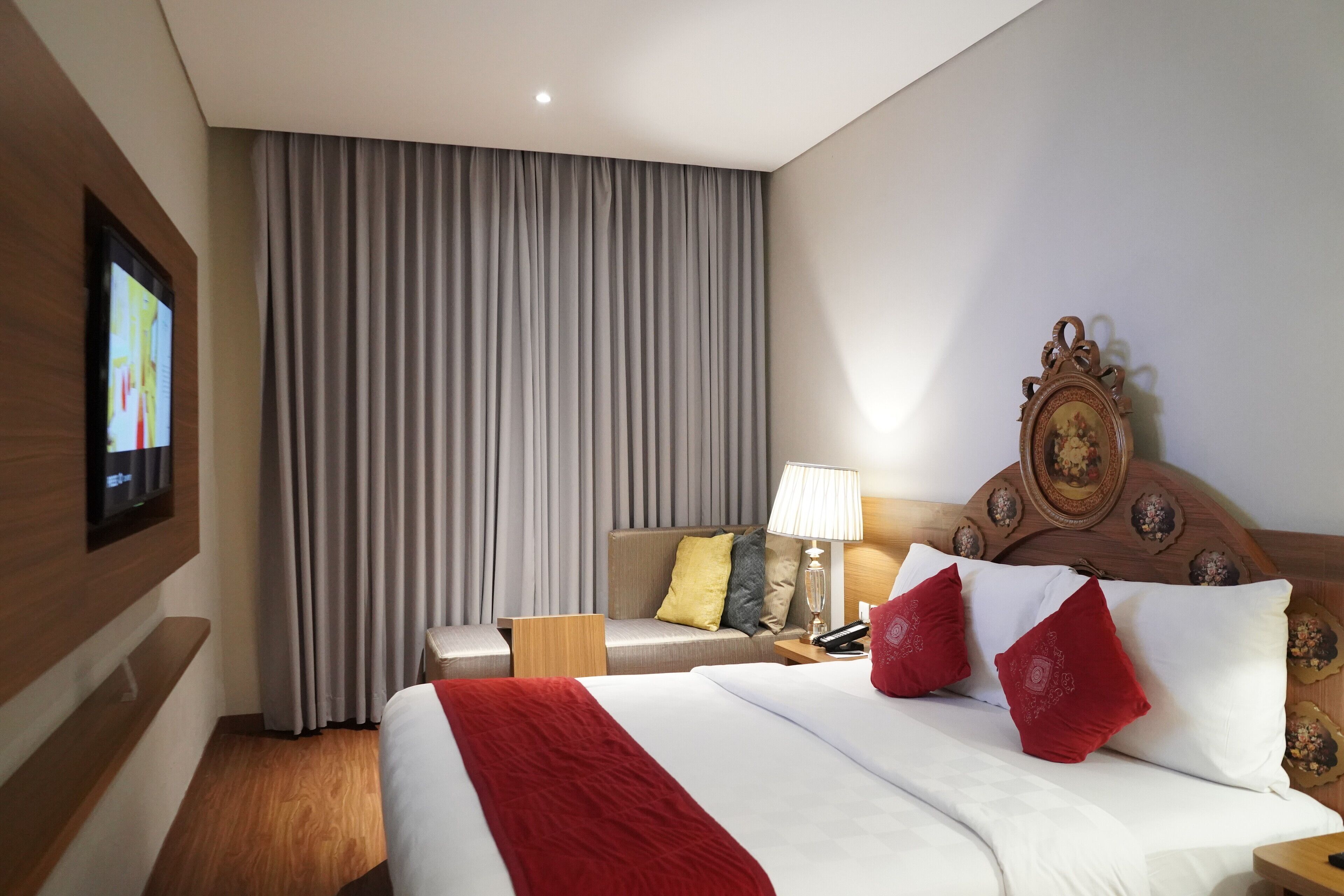 A hotel room with a large bed, a bedside table, a lamp, a television, and a curtain.