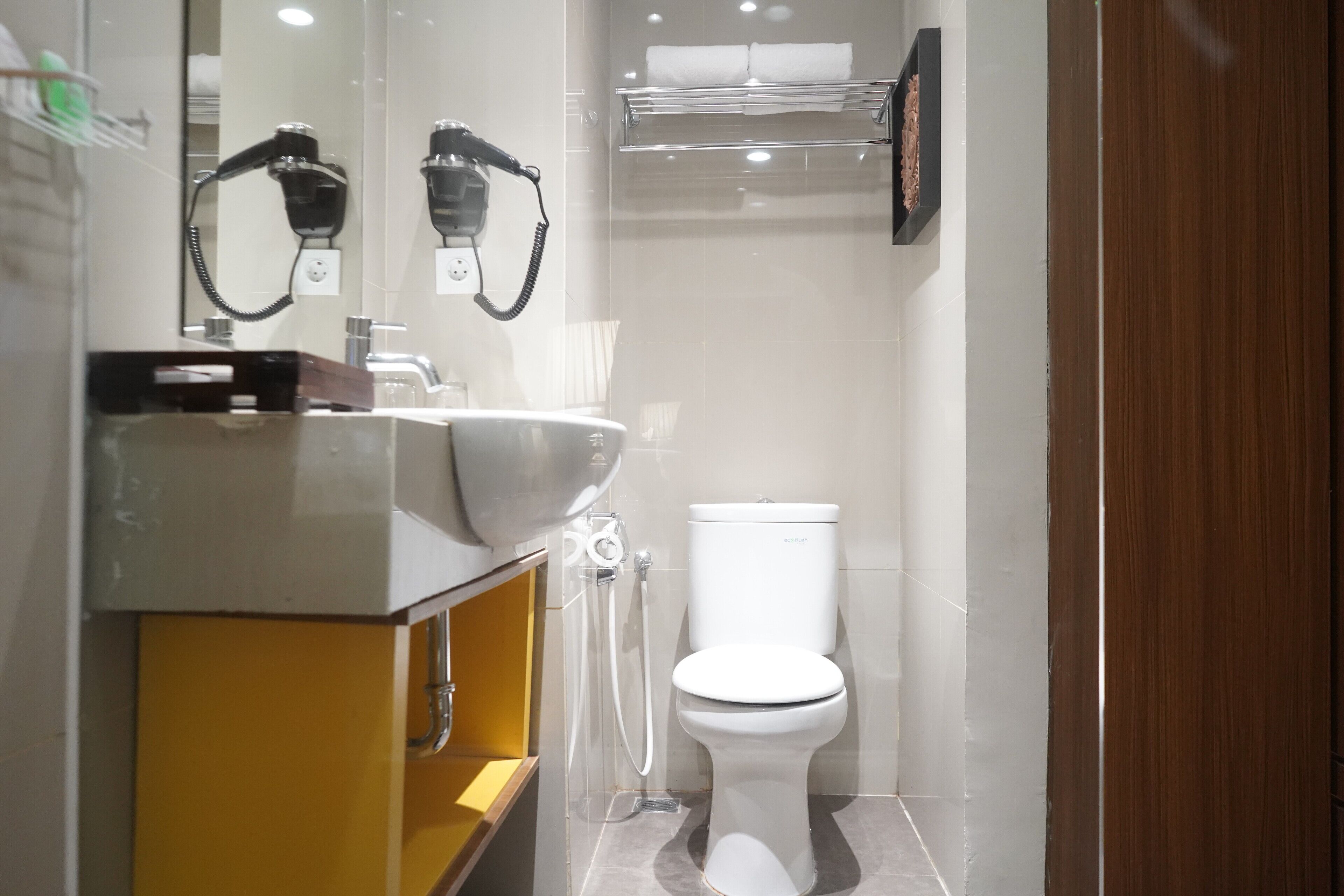 Un baño moderno con inodoro blanco, lavamanos con espejo y un secador de pelo montado en la pared.