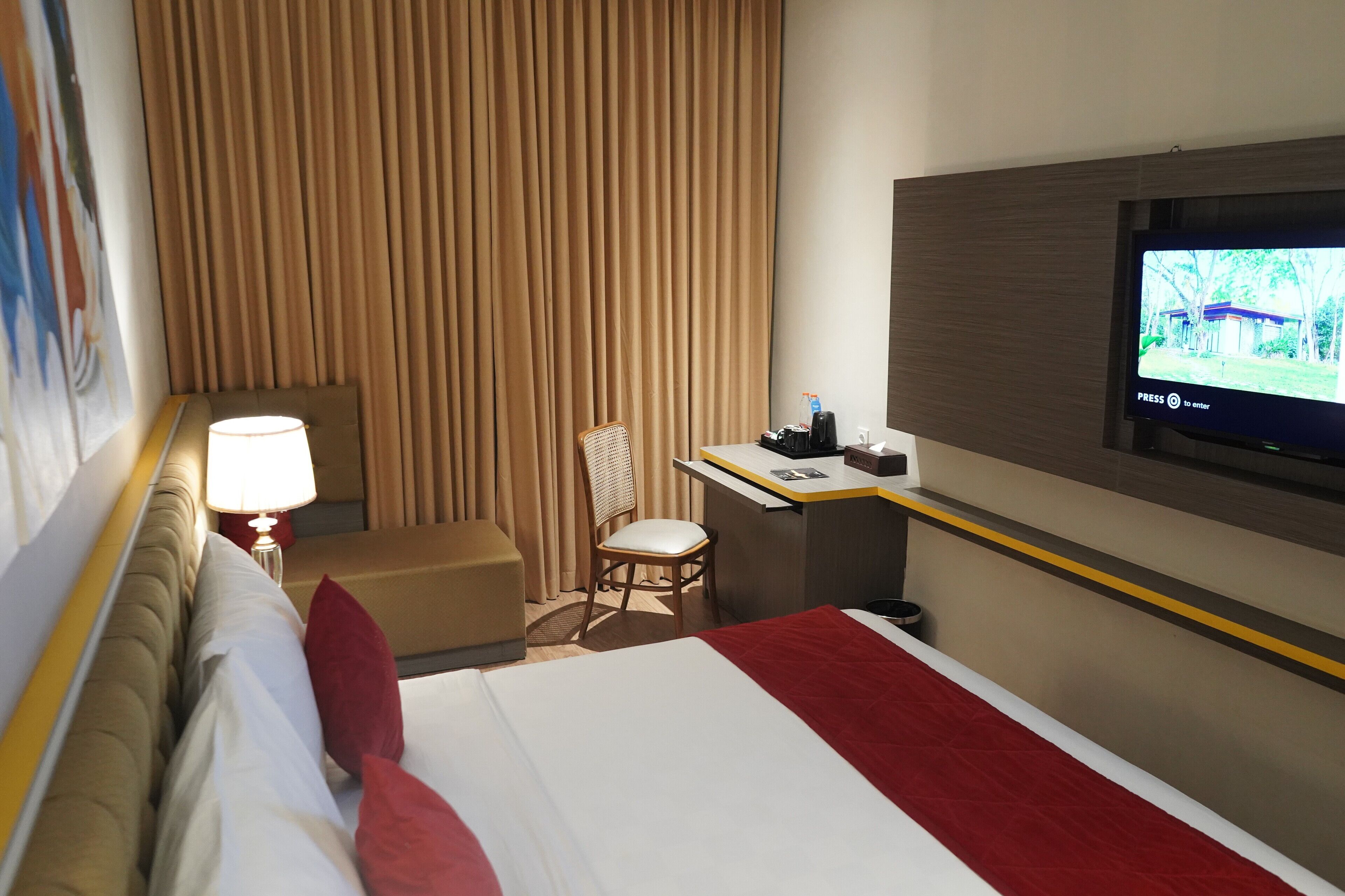 A hotel room with a bed, a desk, a chair, a television, and a window with curtains.