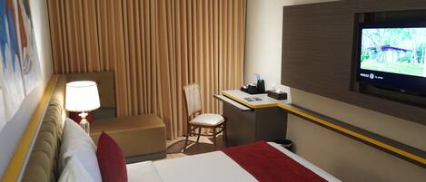 A hotel room with a bed, a desk, a chair, a television, and a window with curtains.