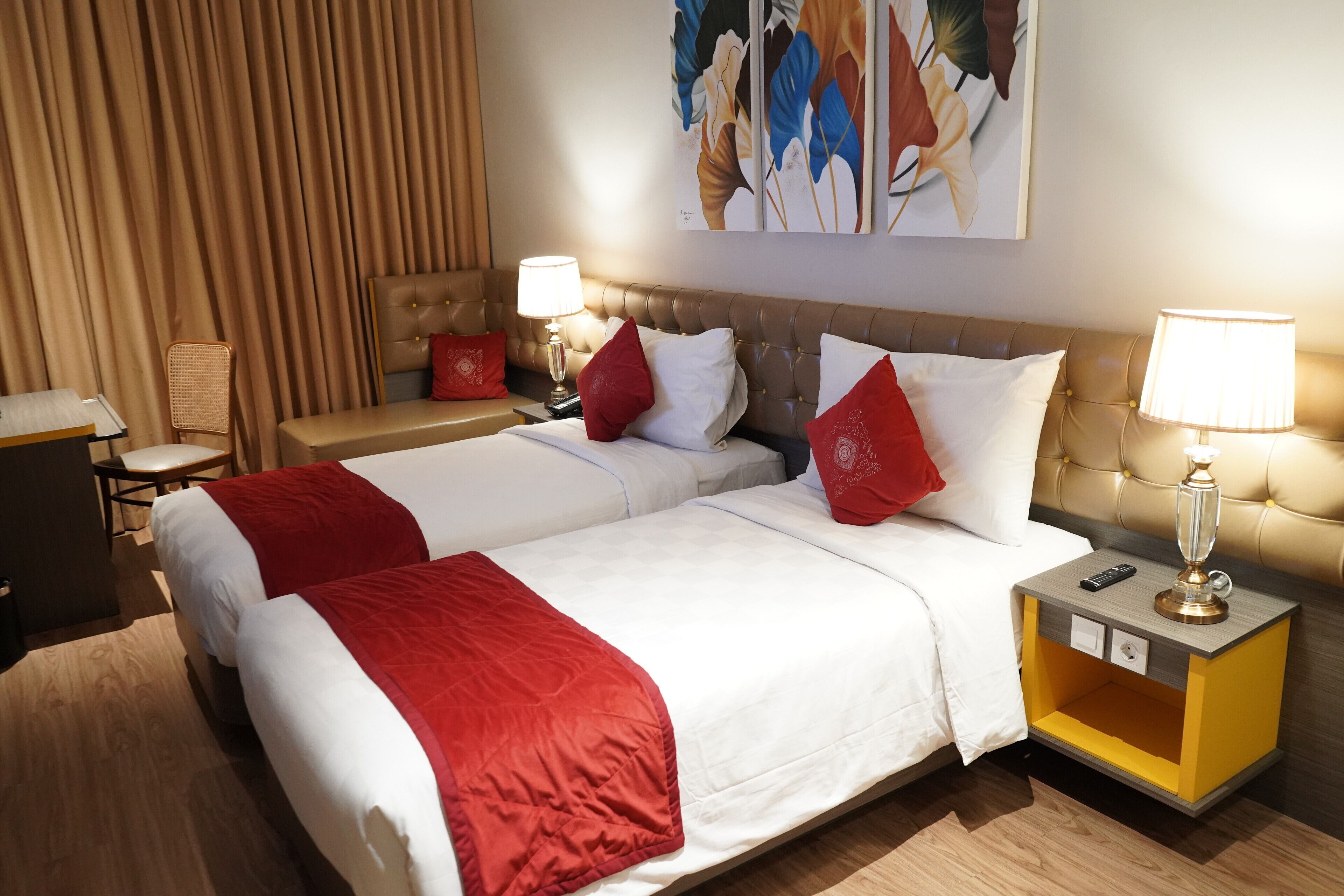 Una habitación de hotel con dos camas, una mesita de noche, una lámpara y un cuadro en la pared.