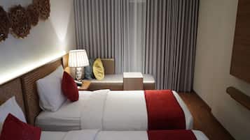 Habitación de hotel con dos camas, una mesita de noche con lámpara, cabecero de madera y una ventana grande con cortinas.