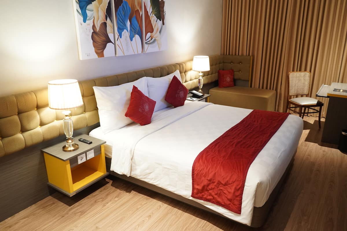 Quarto de hotel com uma cama grande, duas mesas de cabeceira com luminárias, uma cabeceira e uma obra de arte na parede.