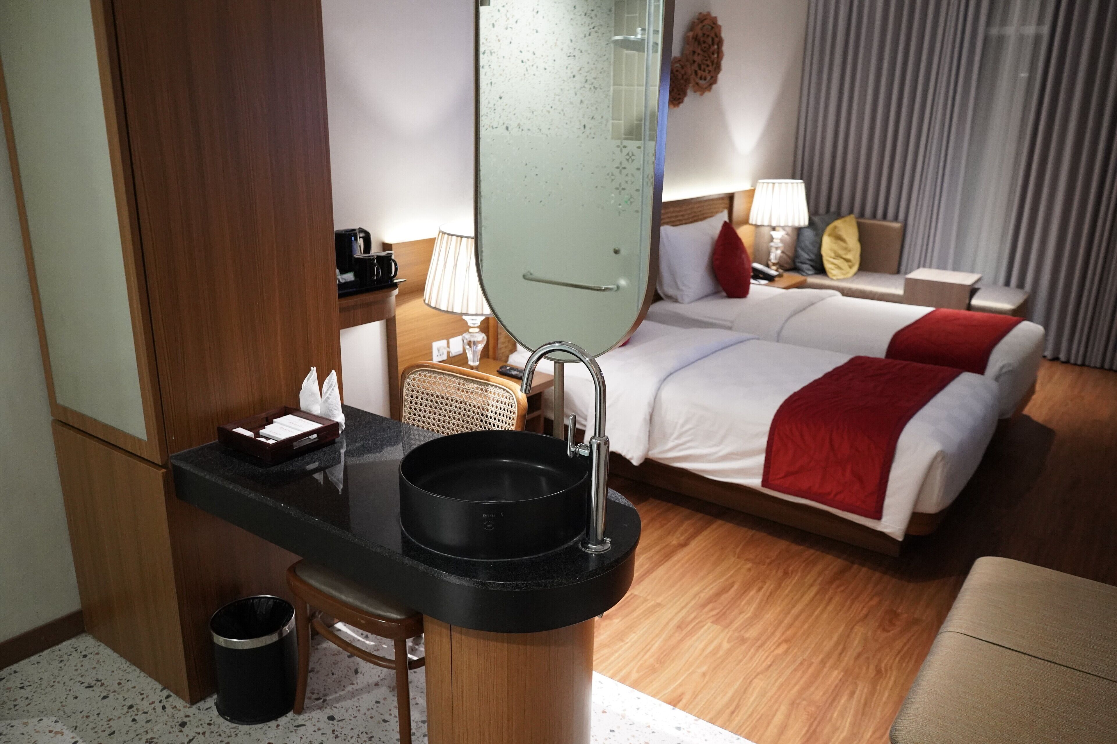 Una camera d'albergo con un letto, una scrivania con lavandino, una sedia, una lampada e uno specchio.