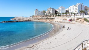 Une plage avec une eau d’un bleu limpide, une digue rocheuse et des bâtiments en arrière-plan.