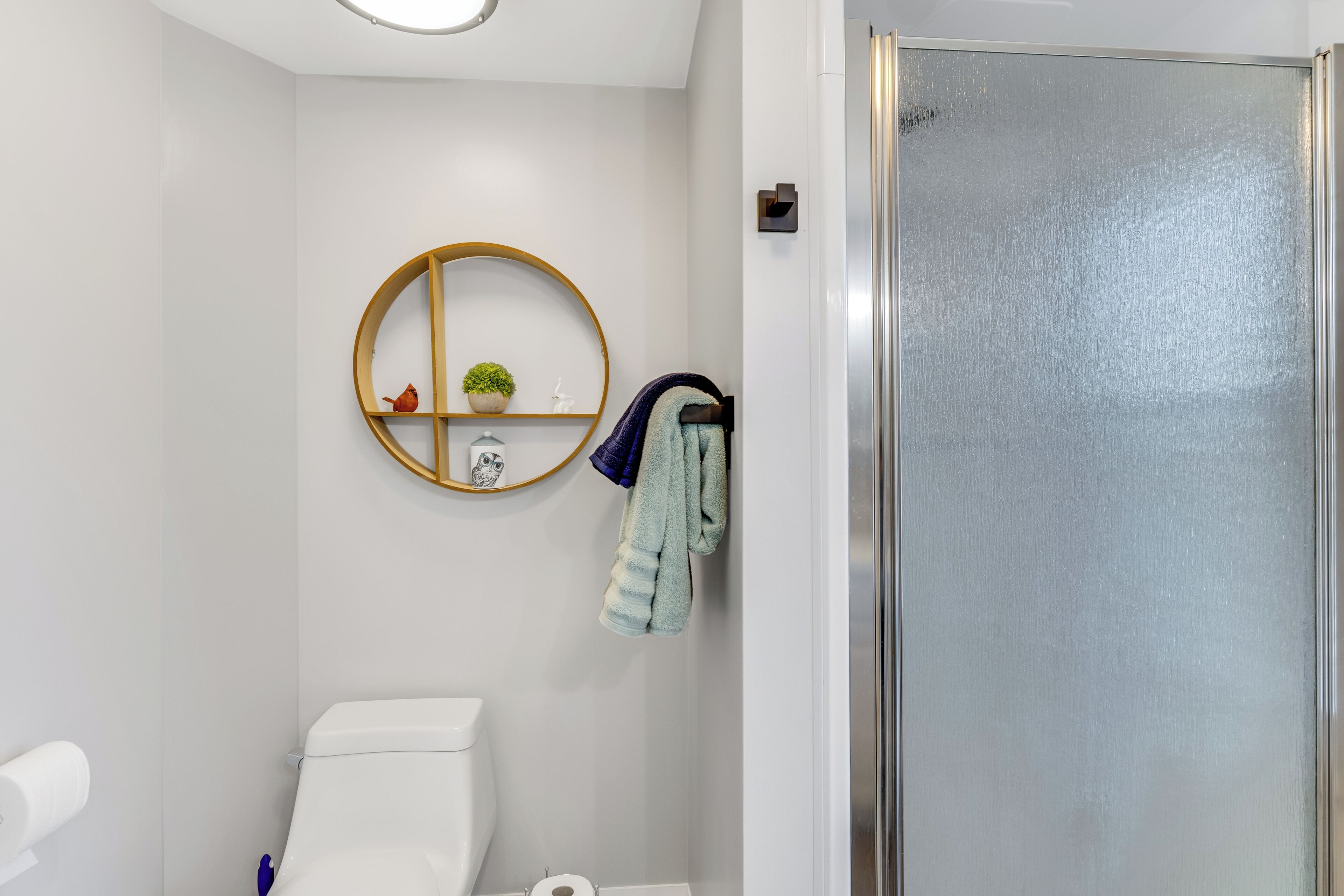 Un bagno con il water, un portasciugamani con asciugamani, uno specchio rotondo e un piccolo ripiano con una pianta.