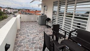 Un balcón con suelo de piedra, una mesa con sillas y vista panorámica de la ciudad.
