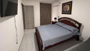 Un dormitorio con cama, televisor montado en la pared, una puerta y un aire acondicionado.