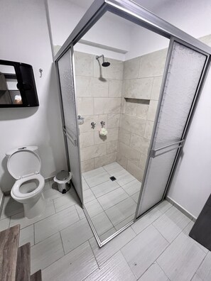 Un baño moderno con ducha de mampara de vidrio, inodoro y lavamanos.