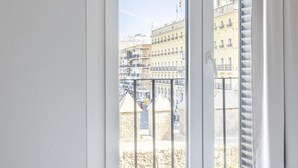 Una camera d'albergo con un'ampia finestra che si affaccia su un panorama urbano con edifici storici e una zona sabbiosa.