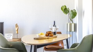 Zona pranzo moderna con un tavolo rotondo, due sedie, un tagliere con cibo, una bottiglia di vino e una pianta.