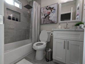 Enjoy a relaxing soak in the bathtub or refreshing shower, with a toilet, sink, and trash can nearby.