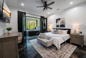 A bedroom with a bed, bedside tables, a ceiling fan, and a view through a glass door to an outdoor area.