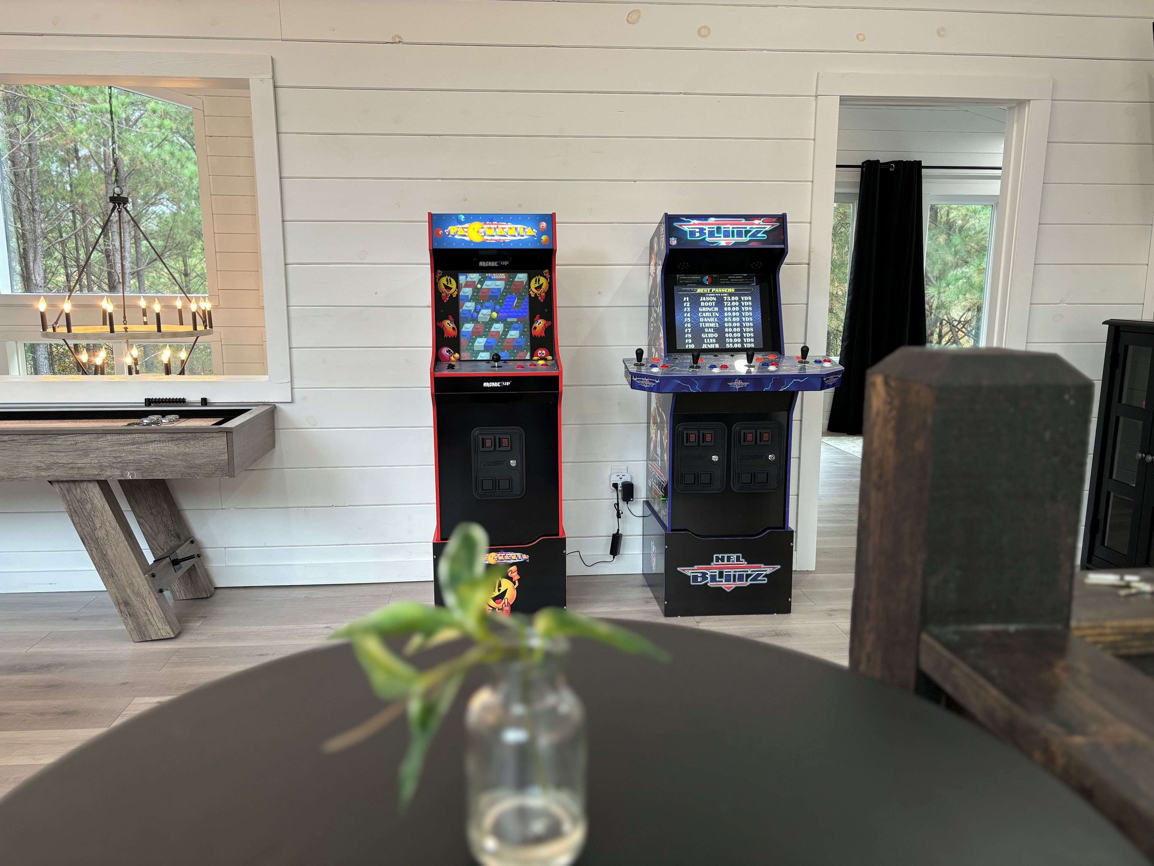 Two arcade machines, a wooden table with candles, and a plant in a glass vase.