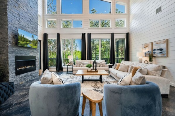 A spacious living room with a fireplace, large windows, and a view of the outdoors.