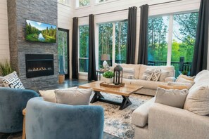 A modern living room with a fireplace, large windows, and a cozy seating area. - NEW Luxe Cabin/4 Private King Bedrooms/Firepit/Creek Nearby/Air Hockey/Arcades (Broken Bow)