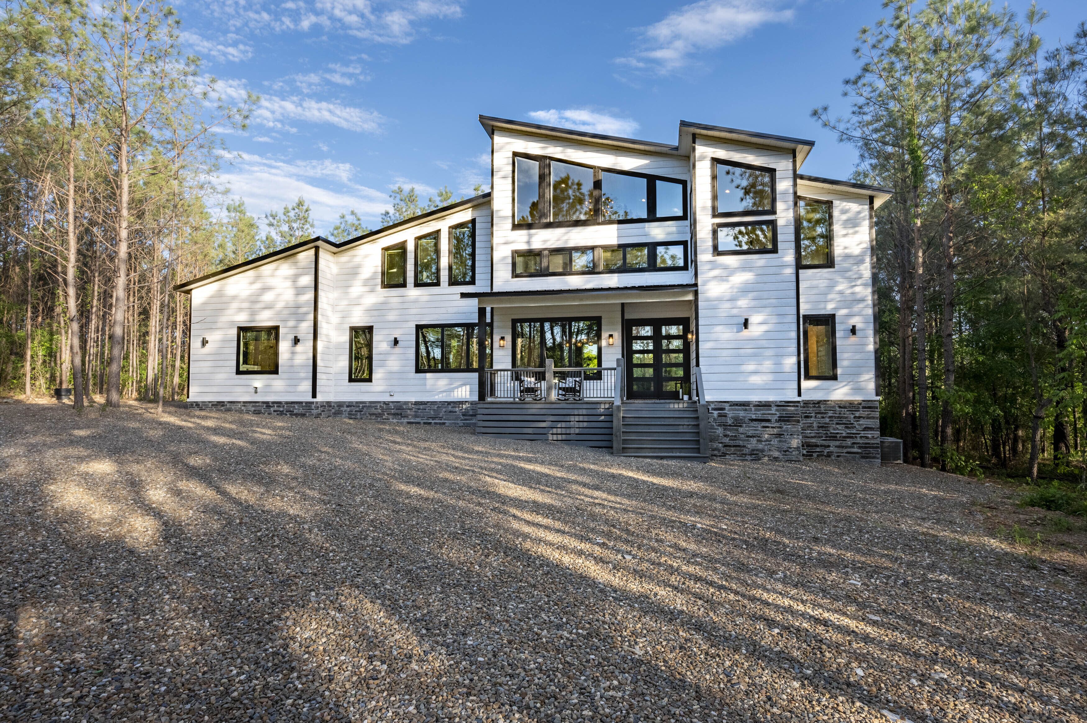 A modern two-story house with a gravel driveway, surrounded by trees.