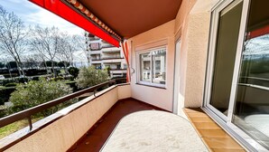 A balcony with a view of a residential area, a sliding glass door, and a red awning. - Apto a 5 min de la playa, Platja d'Aro (Platja d'Aro)