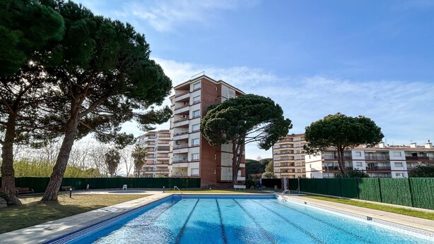 A swimming pool with a clear blue water surface, surrounded by trees and a multi-story building in the background. - Apto a 5 min de la playa, Platja d'Aro (Platja d'Aro)