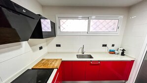 A compact kitchen with a built-in stove, a sink, and red cabinets. - Apto a 5 min de la playa, Platja d'Aro (Platja d'Aro)