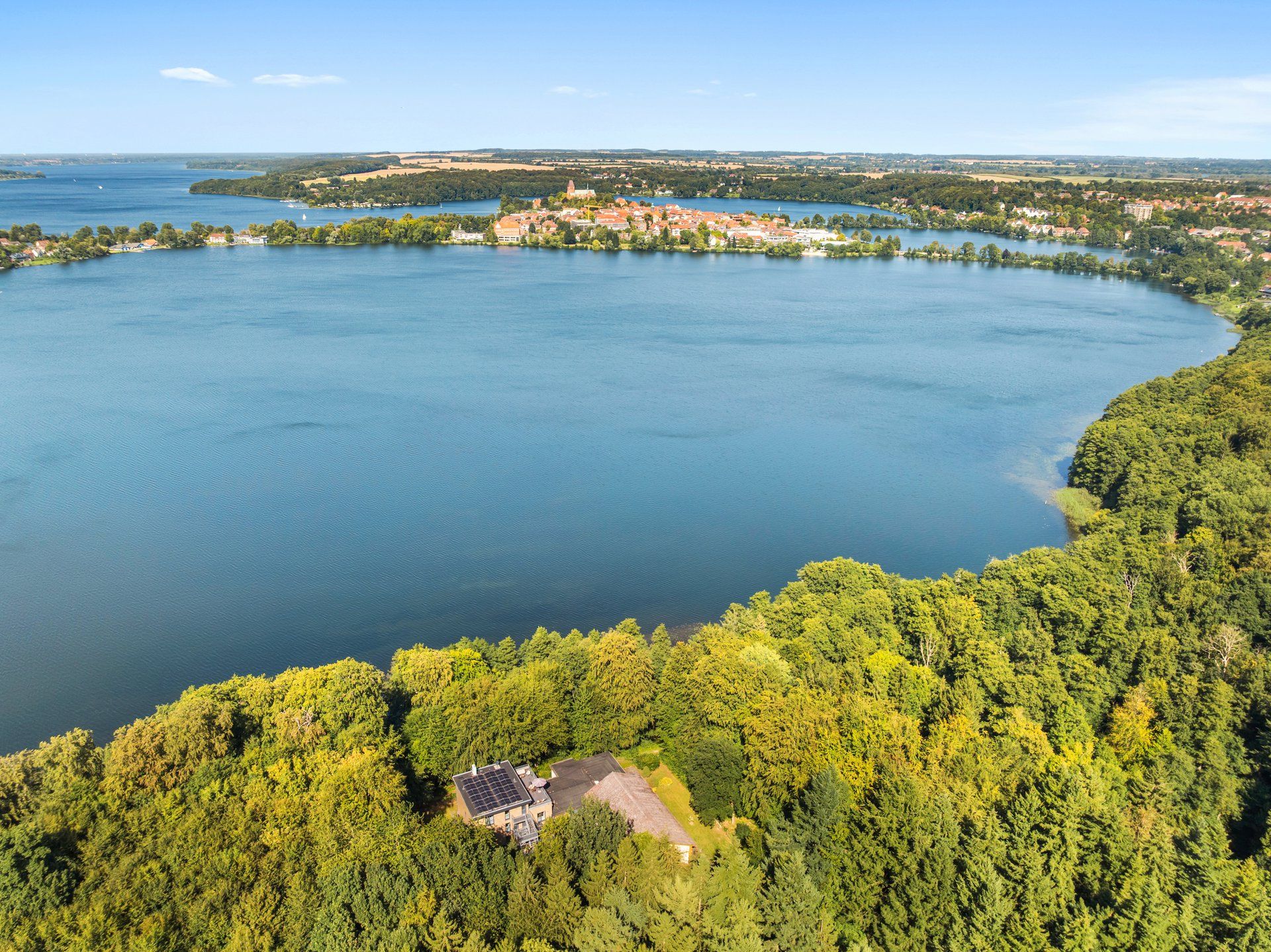 Vista aérea de un lago rodeado de bosque denso y un pequeño poblado con edificios a la vista.