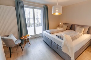 Ein Schlafzimmer mit einem Bett, einem Sessel, einem kleinen Tisch mit Snacks und Blick durch ein Fenster.