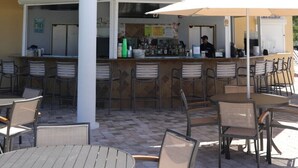 Un área de bar al aire libre con una sección de asientos cubierta, una barra y una pequeña estructura tipo torre en el techo.