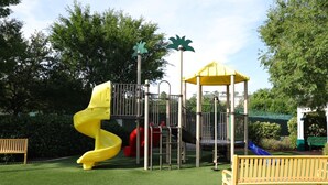 Un parque infantil con un tobogán espiral amarillo, una estructura para escalar y un refugio con toldo amarillo.