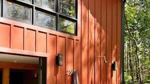 Ein modernes Haus mit großer Holzfassade, ein sichtbares Schlafzimmer mit Bett und kleinem Tisch sowie eine Holzterrasse.