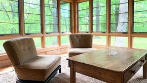 Ein Zimmer mit großen Fenstern, zwei Polstersesseln und einem Holztisch.