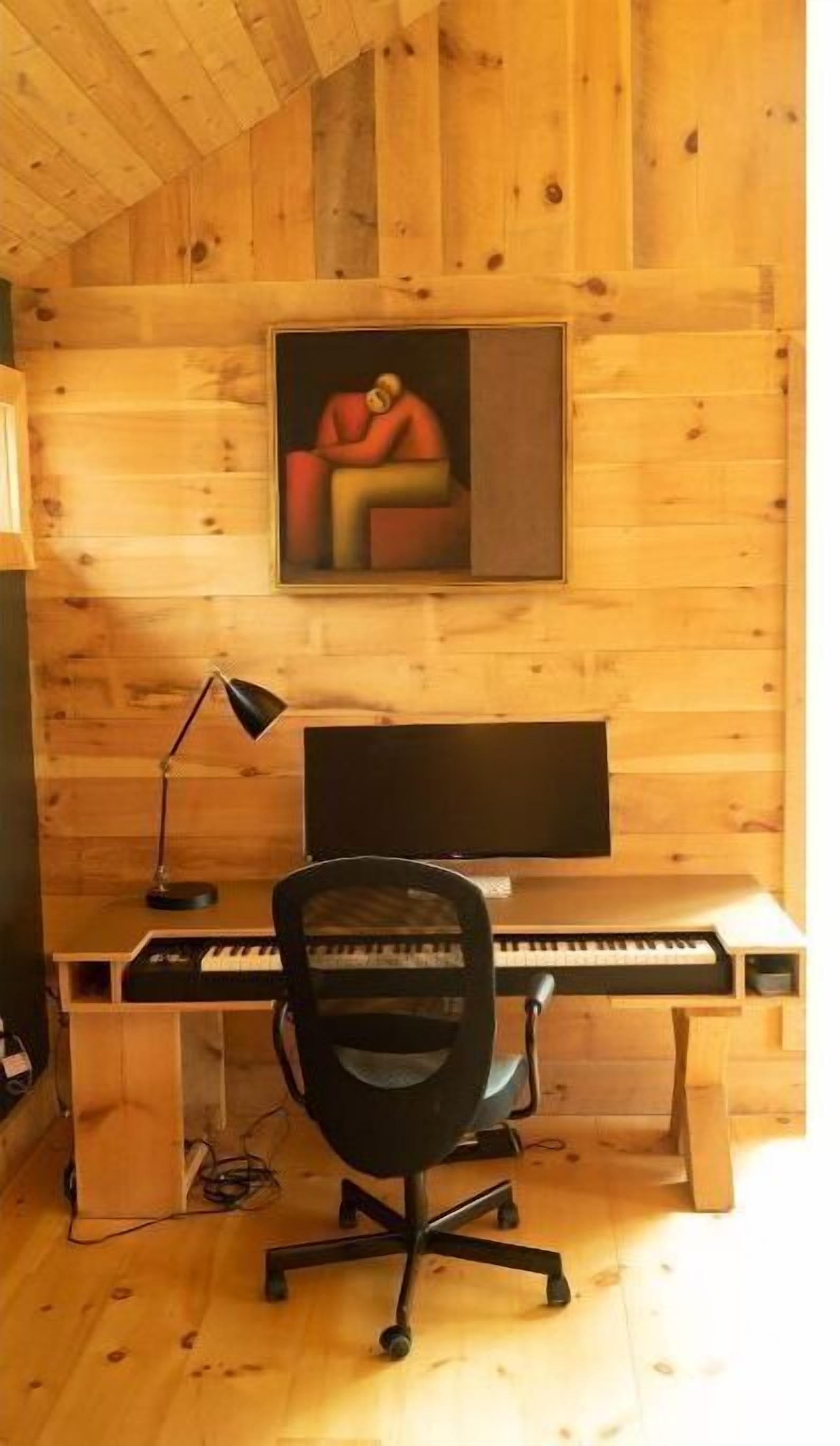 Une pièce aux murs lambrés, avec un bureau, une chaise, un ordinateur et un tableau accroché au mur.