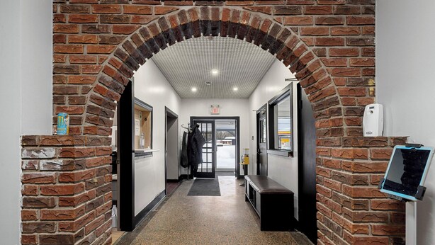 Un couloir orné d’une arche en briques, avec un banc et un panneau d’affichage numérique.