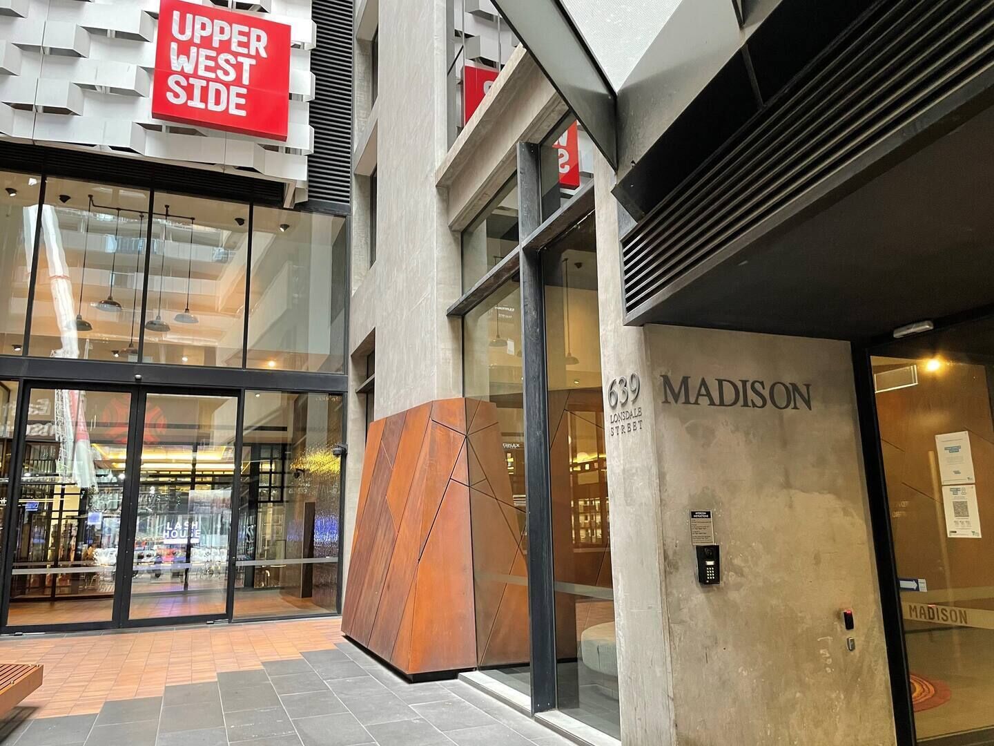 Een modern gebouw met een glazen gevel, een opvallend 'Madison' bord en een 'Upper West Side' aanduiding.