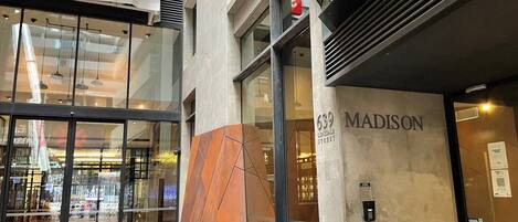 A modern building entrance with a glass facade, a prominent 'Madison' sign, and a 'Upper West Side' sign.
