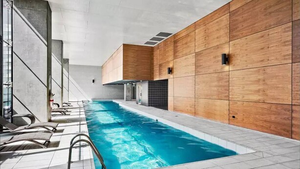 An indoor swimming pool with a modern design, wooden panel walls, and a tiled floor.