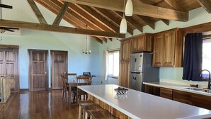 A spacious kitchen with wooden cabinets, a large island, and a dining area with chairs. - A Quiet East End Retreat. Ocean view with a private pool and custom water slide! (Bay Islands Department)