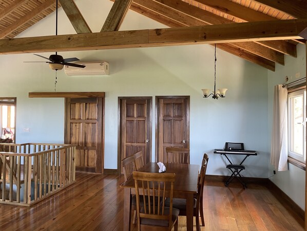 A spacious dining area with wooden flooring, a high ceiling with exposed beams, and a ceiling fan.
